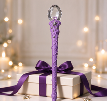Cargar imagen en el visor de la galería, Magic wand placed on a gift box, adorned with purple ribbon and star ornaments, with warm blurred lights in the background.
