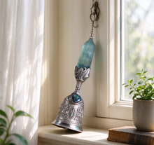 Charger l'image dans la galerie, Silver filigree crystal bell hanging by a bright window with sheer curtains, soft afternoon light, small potted plants and a vintage book on the windowsill – cozy fantasy home décor piece