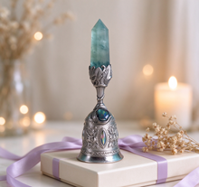 Charger l'image dans la galerie, Crystal fluorite bell ornament resting on a gift box tied with soft lavender ribbon, dried flowers and warm bokeh lights in the background – elegant present for crystal and mindfulness lovers