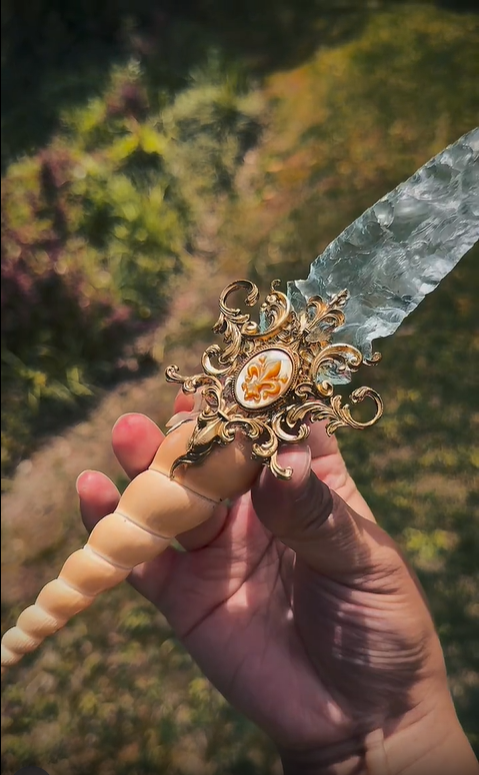 Hand holding the unique Crystal Ritual Dagger, displaying the full length and ergonomic design of the fossil and glass handle