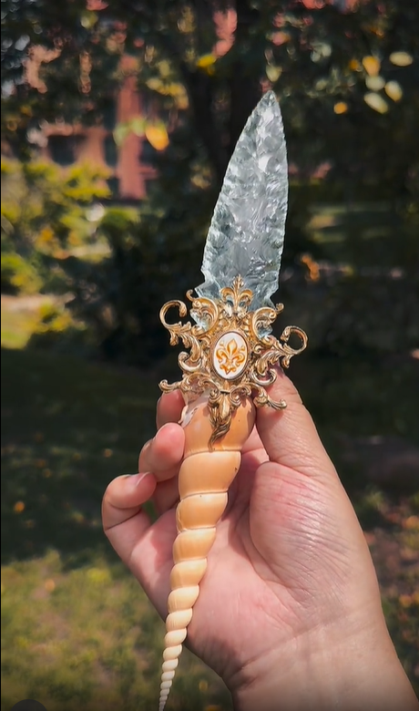 Hand holding the unique Crystal Ritual Dagger, displaying the full length and ergonomic design of the fossil and glass handle