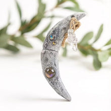 Load image into Gallery viewer, Mystical crescent moon charm displayed against a dark background with forest greenery. Features embedded healing crystals and a raw quartz point, perfect for Wiccan rituals and connecting with earth energy.